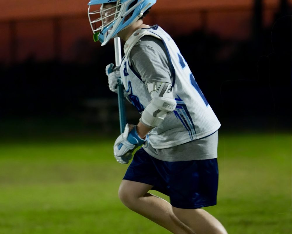 Lacrosse player running with a stick during a night game